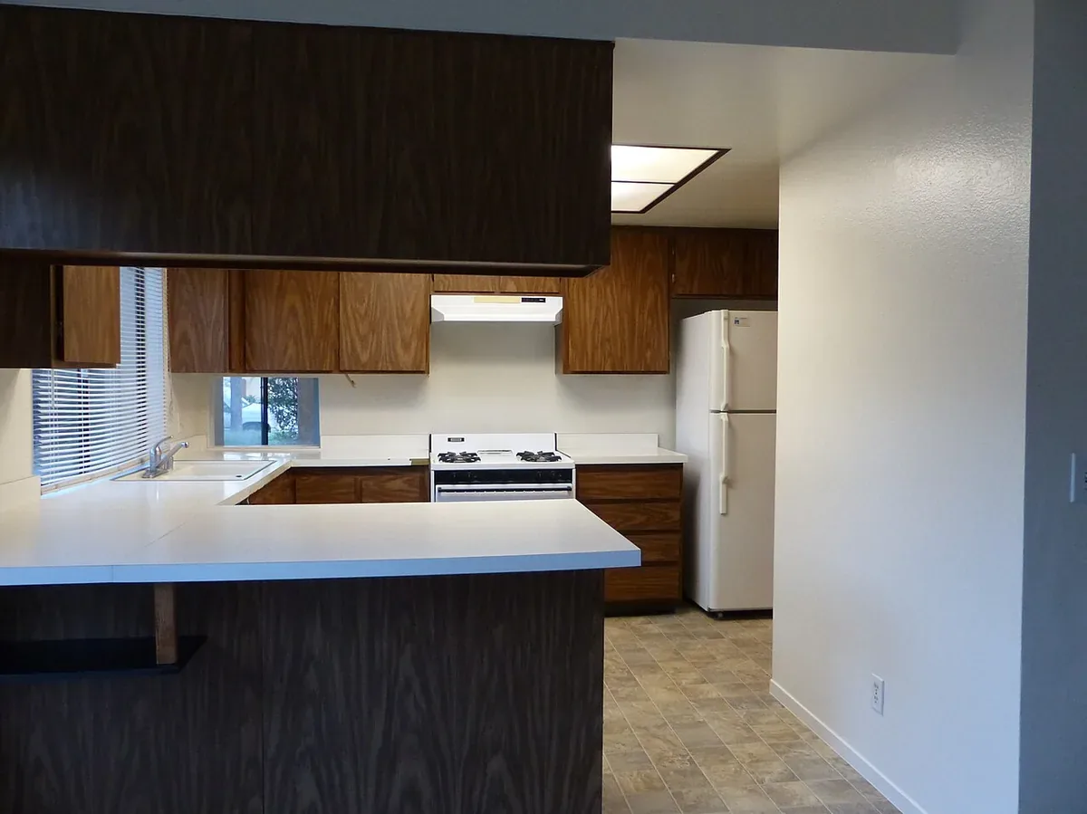 Dated dark woodgrain laminate kitchen cabinets and white laminate counters in a California house, typical of the kitchens replaced in Santa Maria