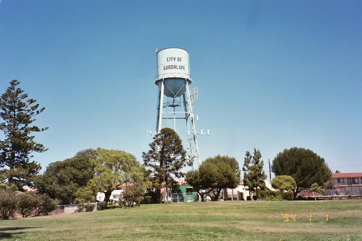 The City of Guadalupe water tower rising above trees and rooftops in Guadalupe CA, west of Santa Maria