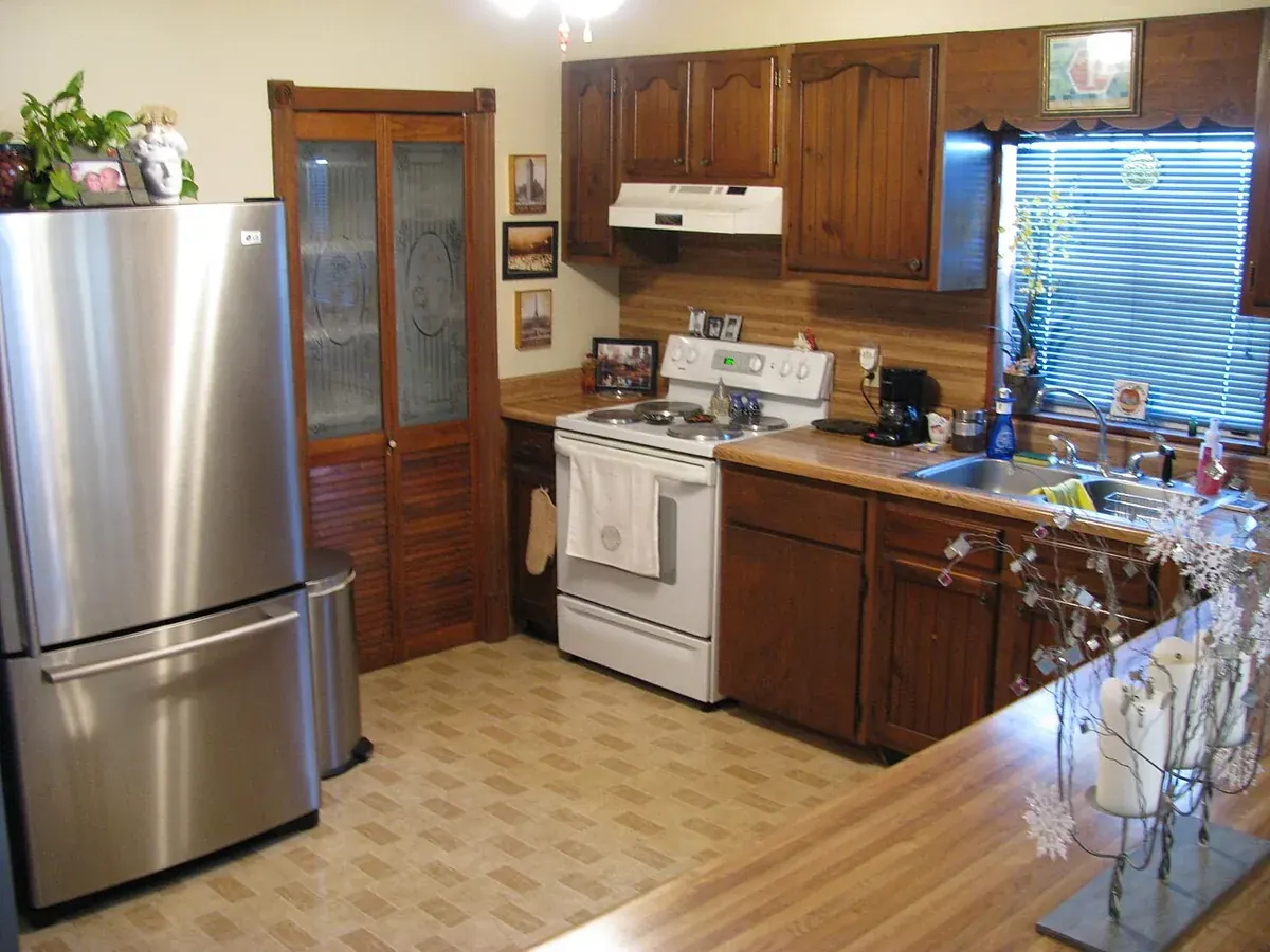 Lived in kitchen with dark stained raised panel wood cabinets, wood laminate counters and a stainless refrigerator, a strong candidate for cabinet refacing