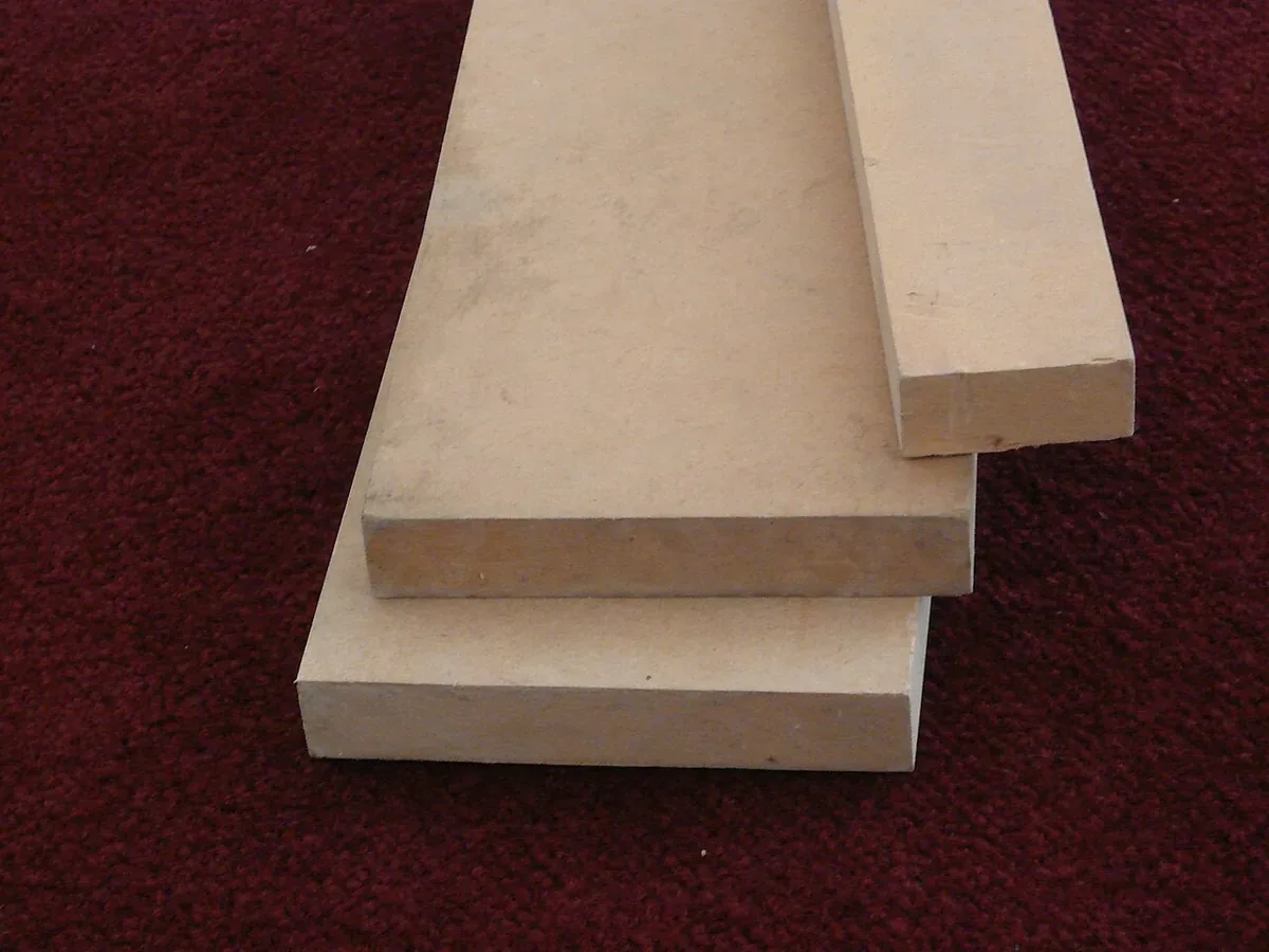 Three cut lengths of plain medium density fibreboard stacked on a carpet, showing the uniform brown core and smooth faces