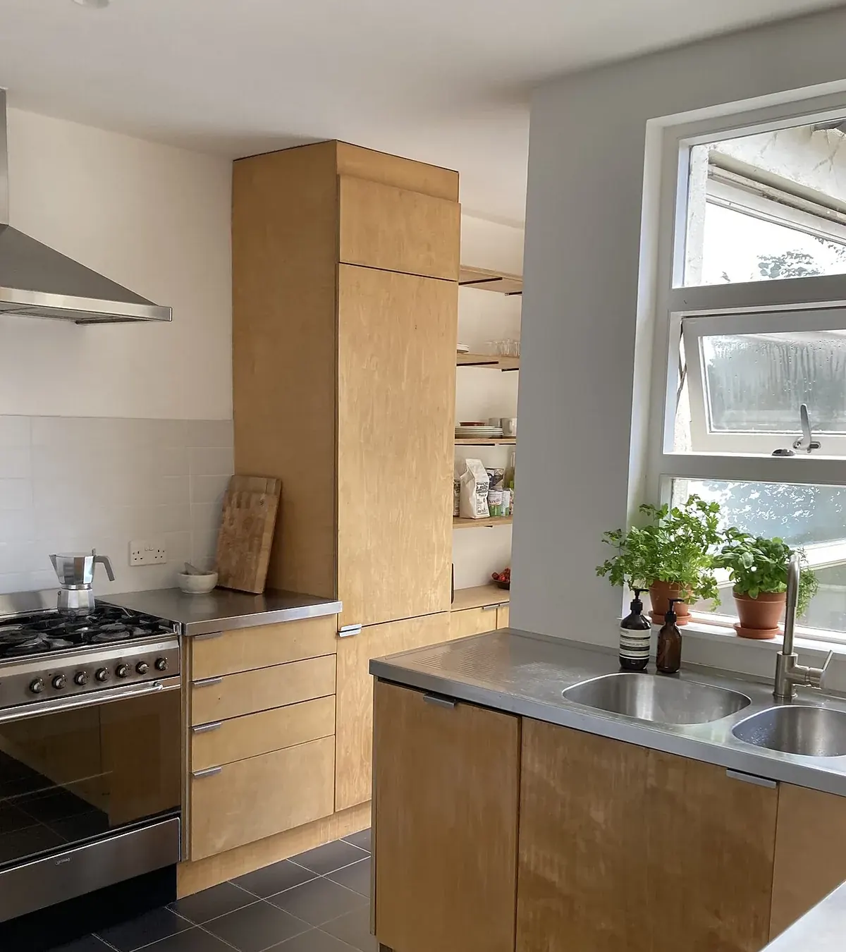 Birch plywood kitchen cabinets with a tall pantry run and stainless counter, showing exposed plywood edges