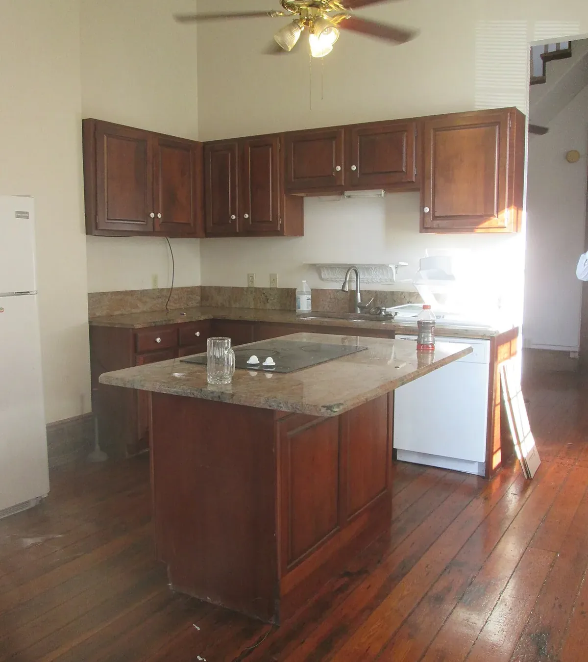 Kitchen with dark stained raised panel cherry cabinets and a matching island under a granite top, on an old plank floor