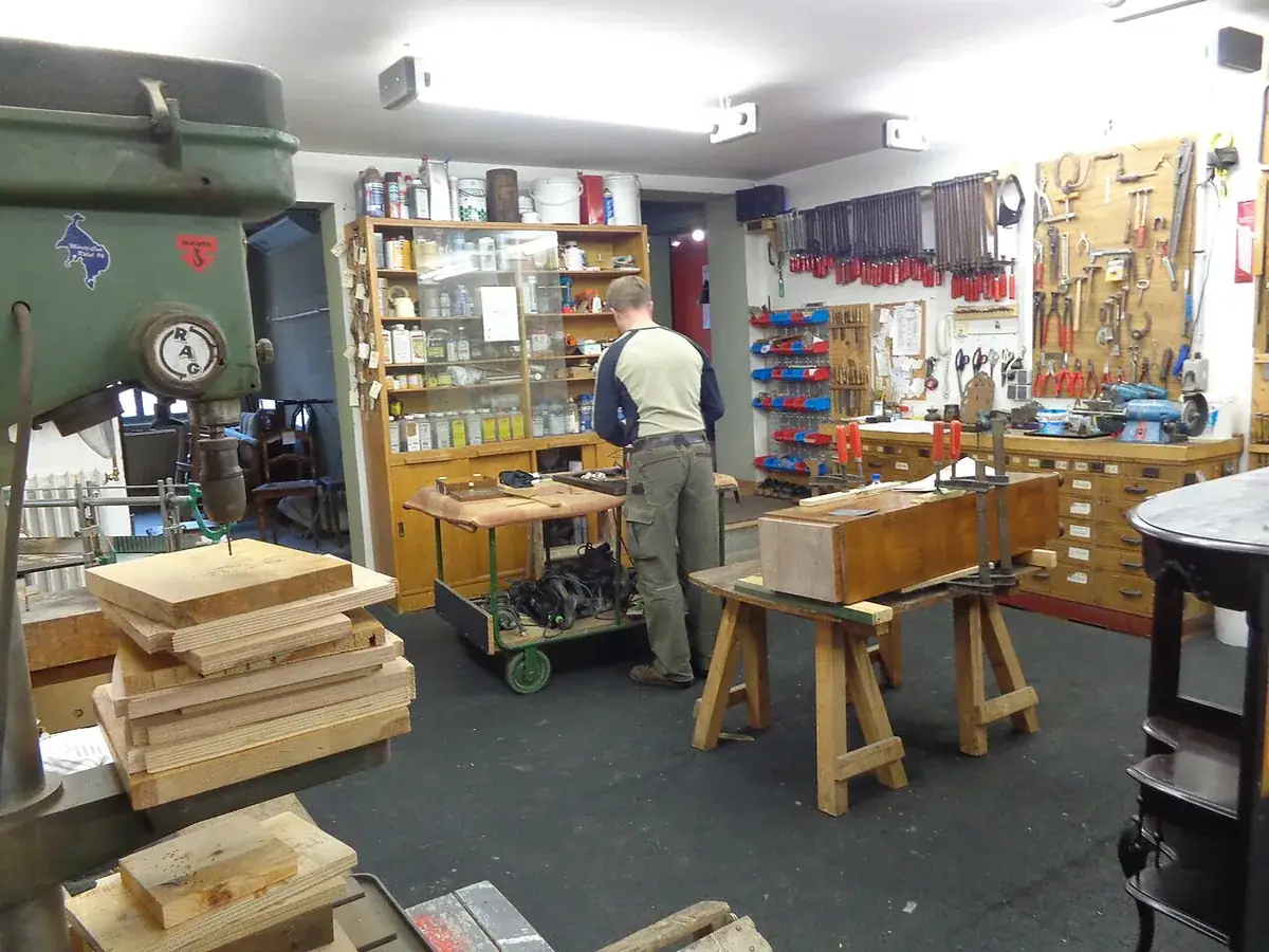 Small cabinet shop with a pillar drill, hand tools racked on the wall and a glued up cabinet carcass clamped on sawhorses