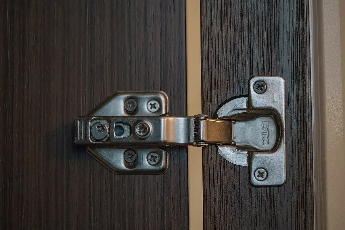 Close up of a concealed soft close cabinet hinge mounted on a dark woodgrain cabinet door